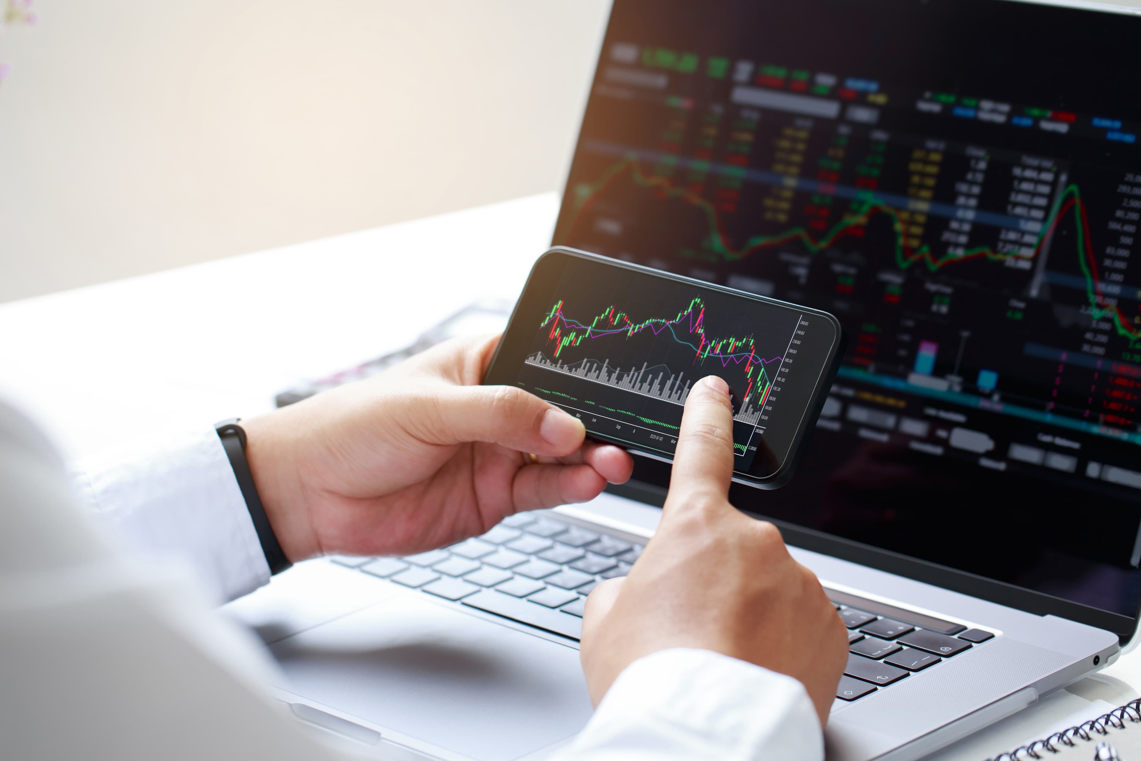 Primer plano de trader sosteniendo móvil con gráficas de mercado en rojo mostrando señales de revenge trading