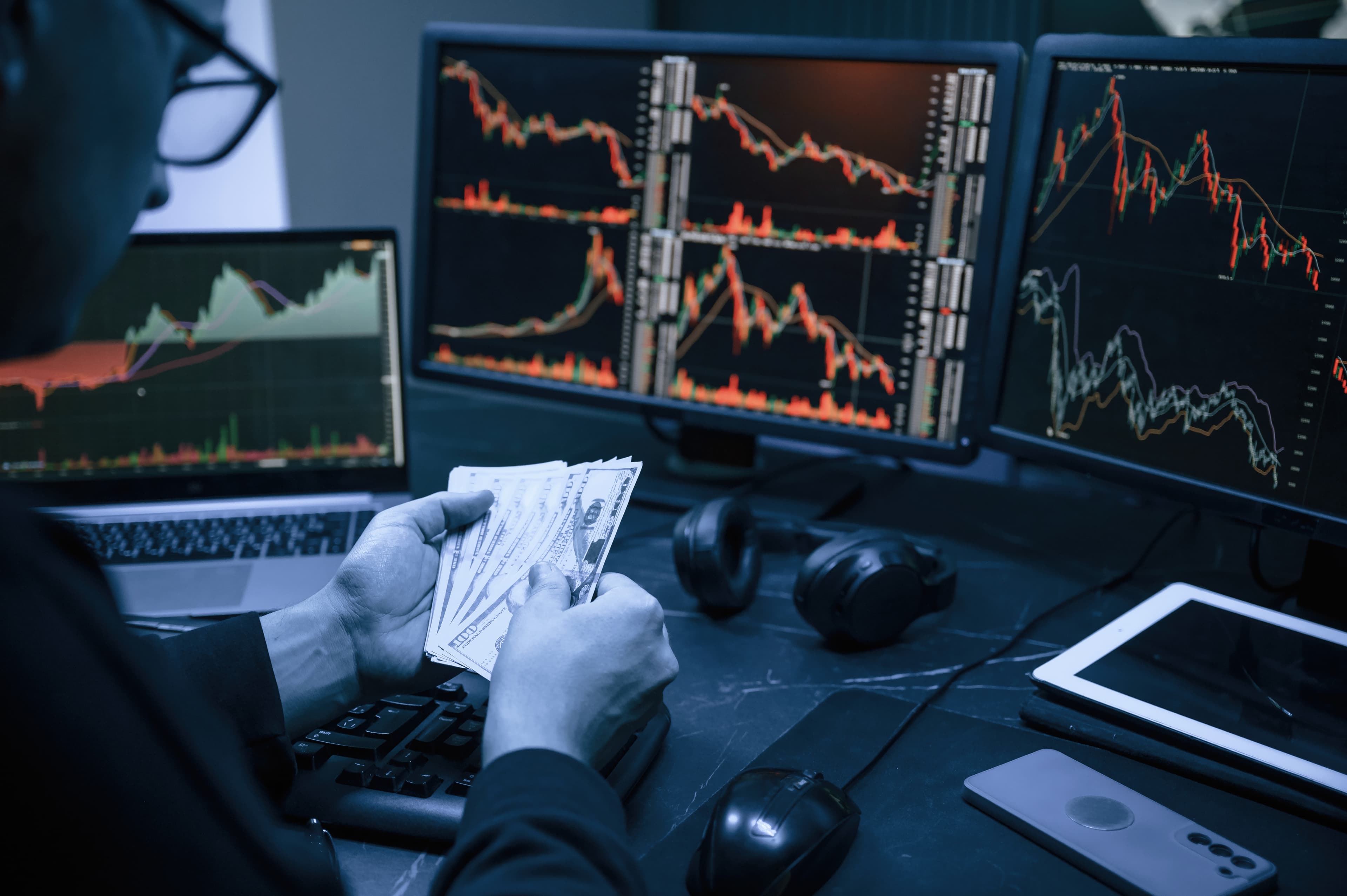 Trader sosteniendo dinero frente a múltiples pantallas de trading representando las consecuencias del revenge trading