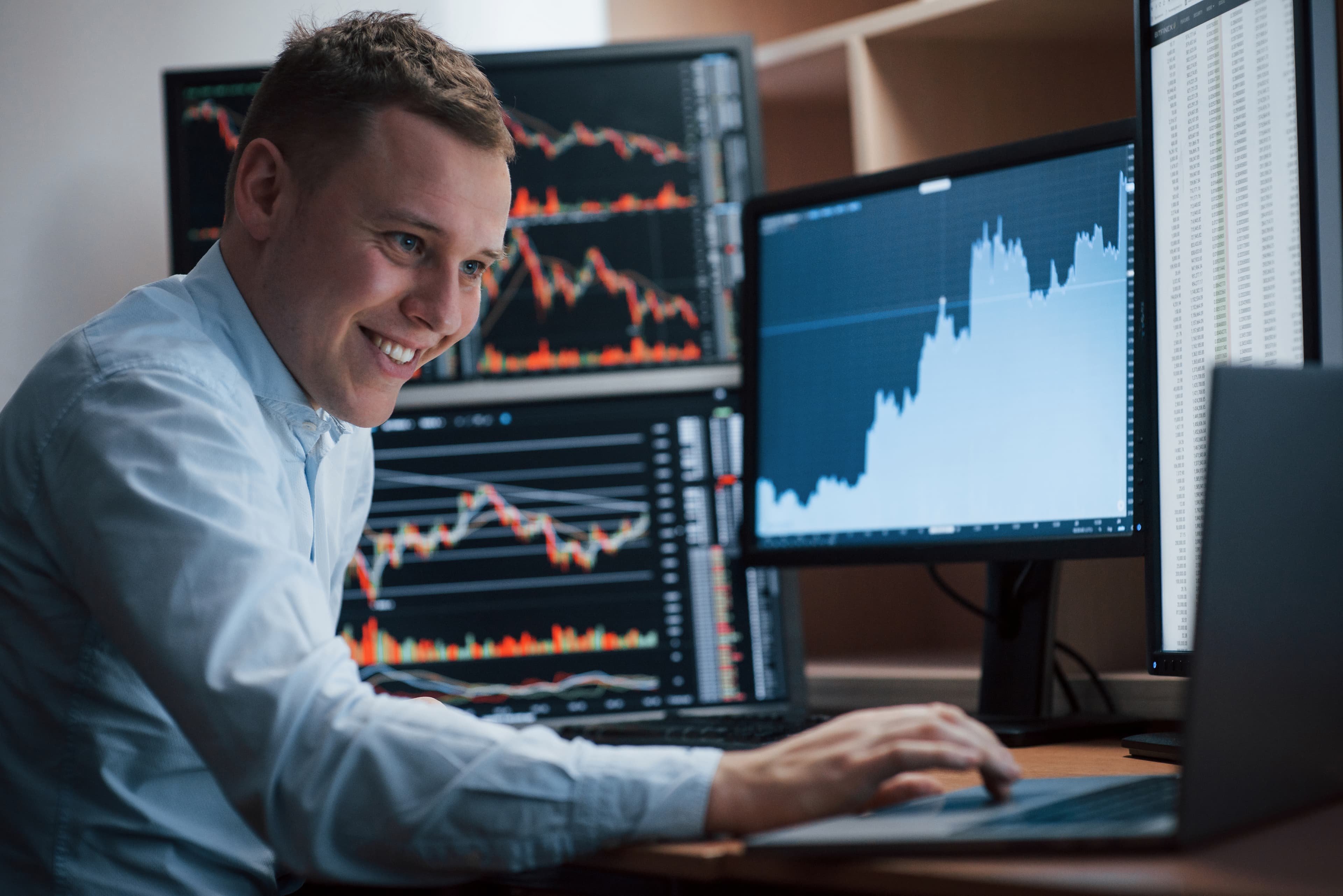 Smiling trader at multi-monitor workstation after successfully passing TopStep evaluation